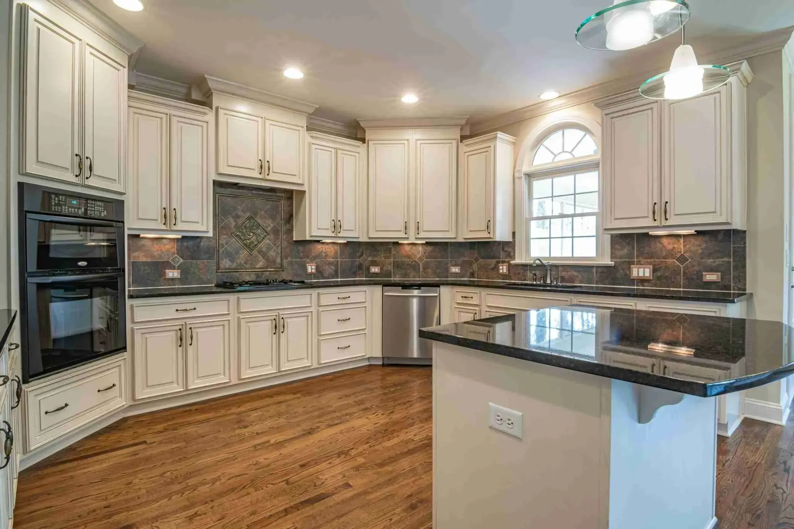 Cream kitchen with dark granite countertops, slate backsplash and a large island