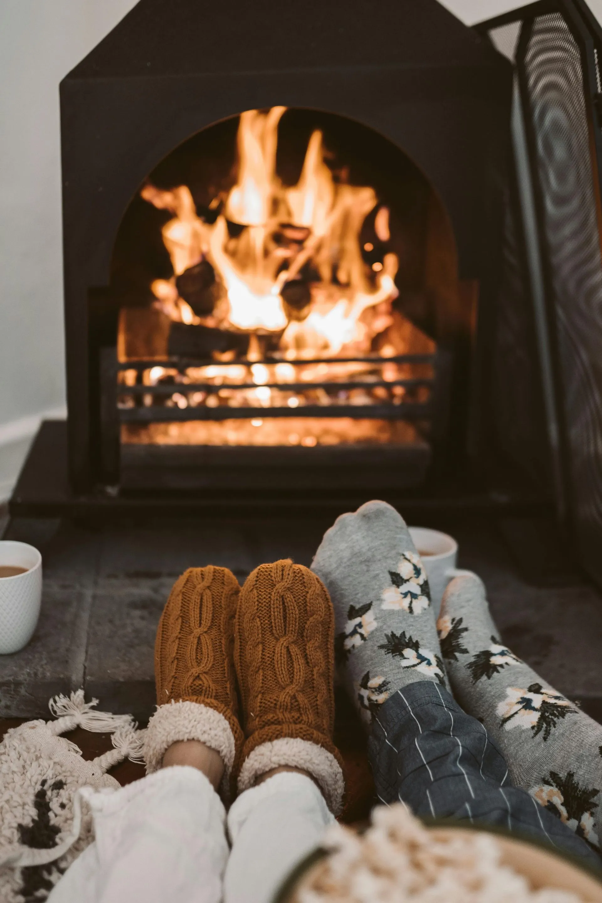 Two people relaxing with their feet up in front of a lit fireplace