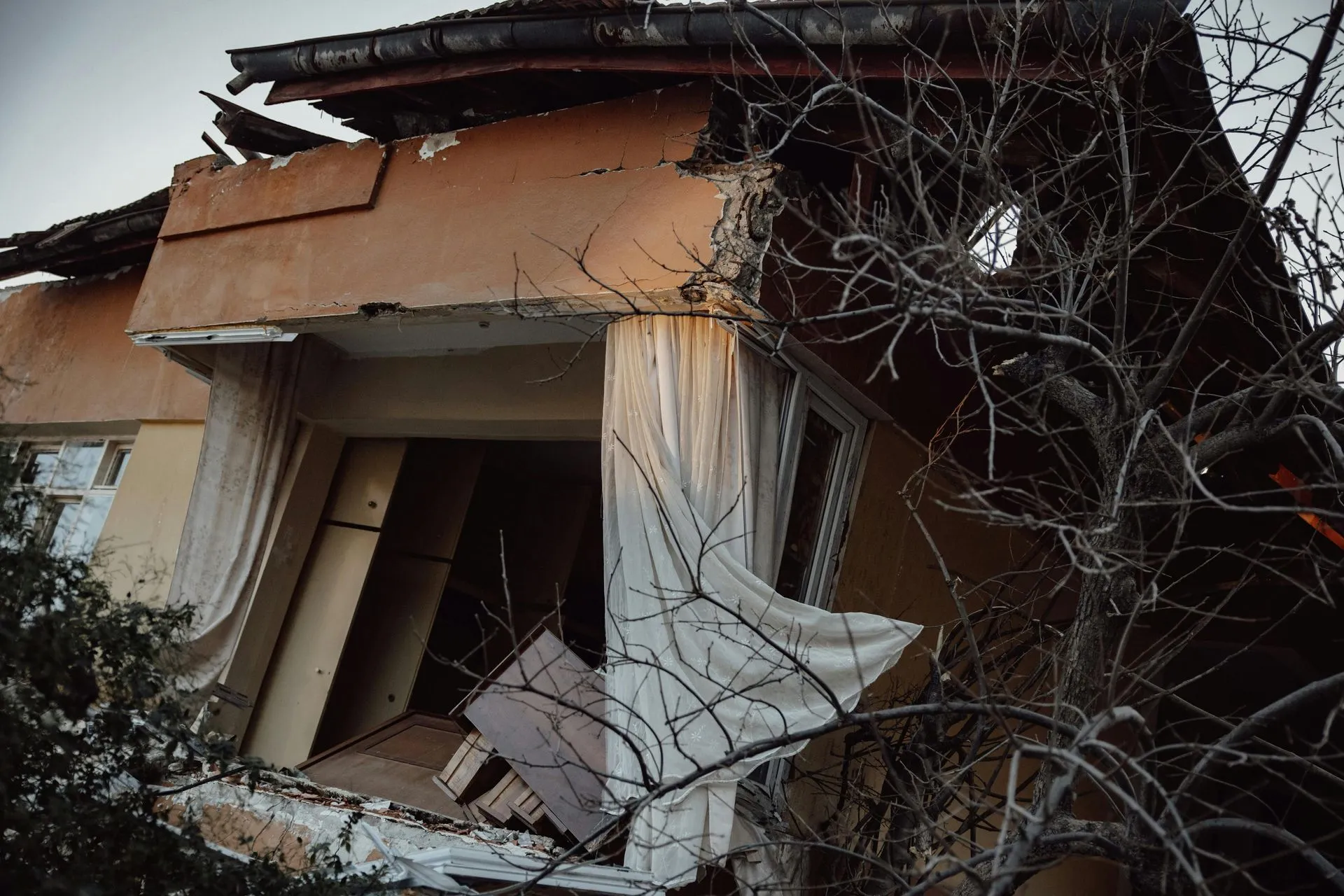 House with a collapsed exterior wall and scattered debris after storm damage
