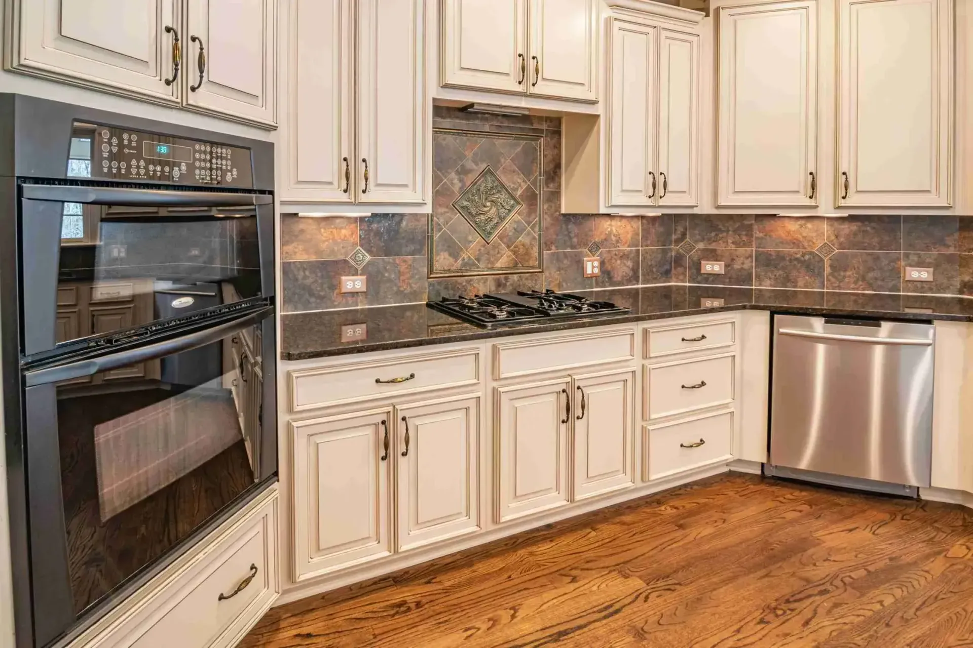Antique white kitchen with double wall ovens, gas cooktop and slate tile backsplash