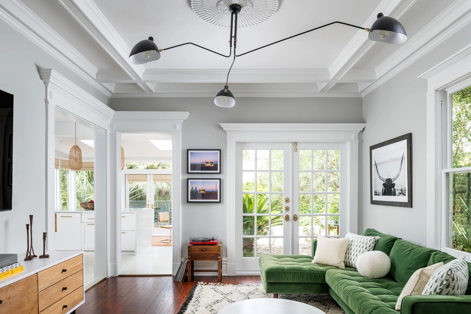 White den with a green velvet sofa, coffered ceiling and French doors