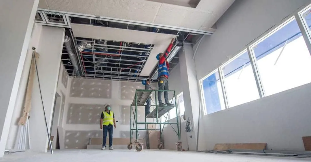 Worker on a scaffold rebuilding a commercial ceiling grid after water damage