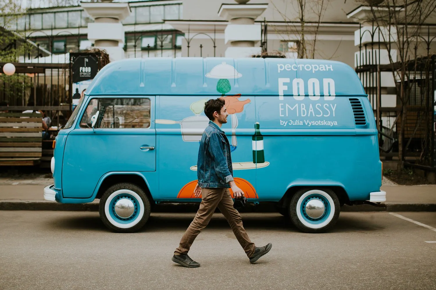 Man walking past a vintage light blue van parked on a city street