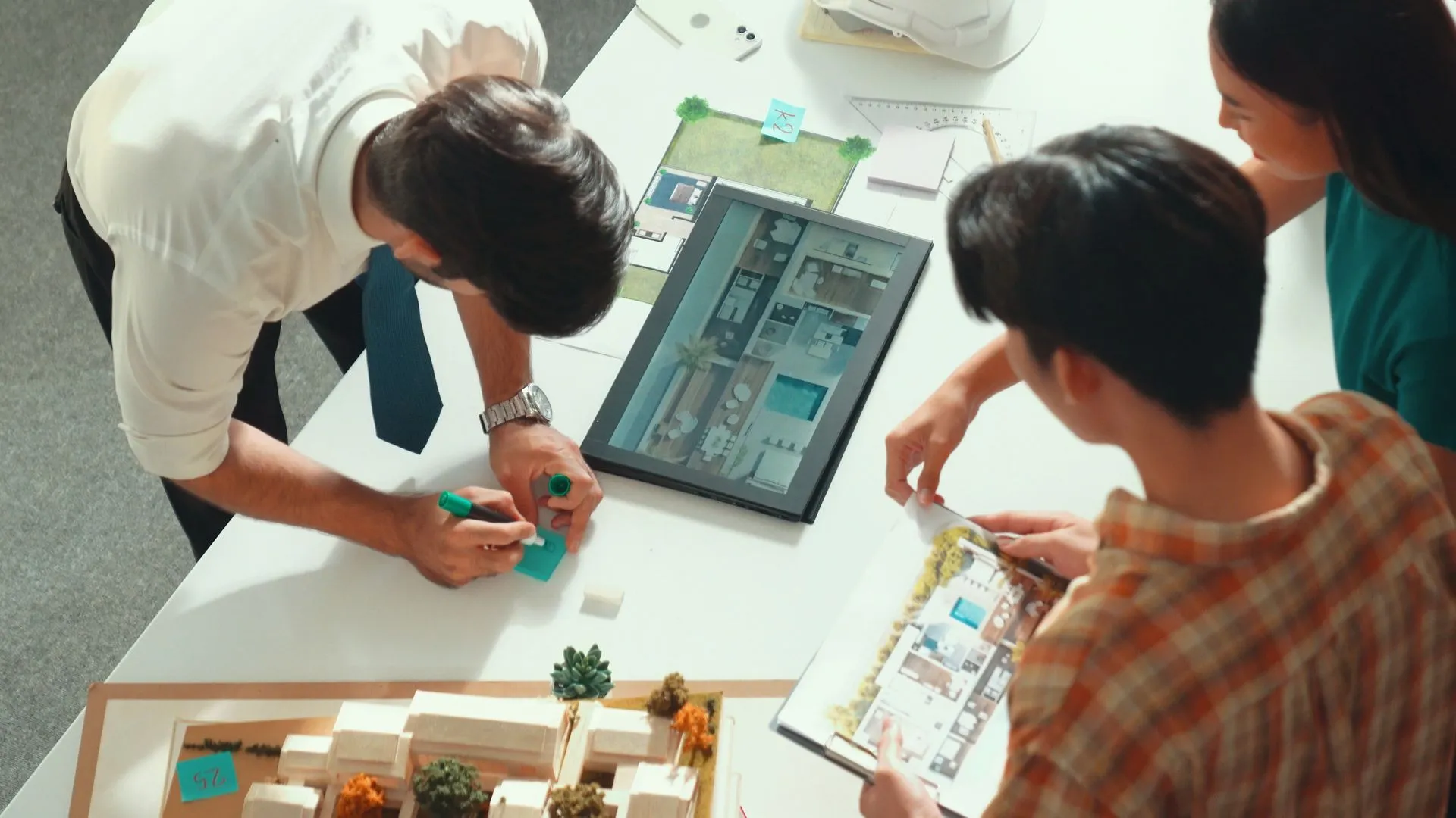 Team reviewing a scale model of a house alongside a tablet and floor plans