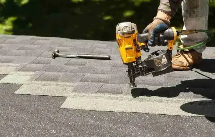 Gloved hand using a coil nail gun to fasten asphalt roof shingles