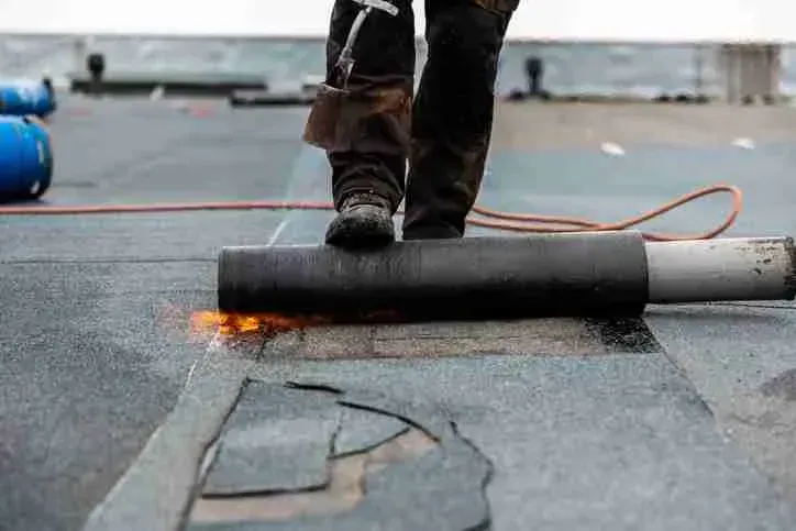 Roofer torch-applying a modified bitumen membrane on a flat commercial roof