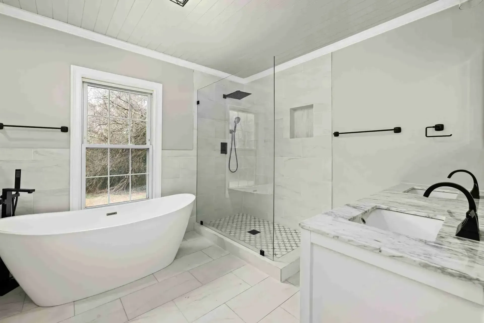 White bathroom with a freestanding tub, glass shower and marble-top vanity
