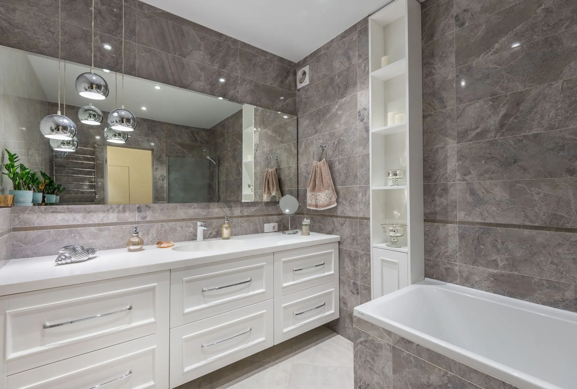 Gray tile bathroom remodel with a white double vanity, pendant lights and built-in tub