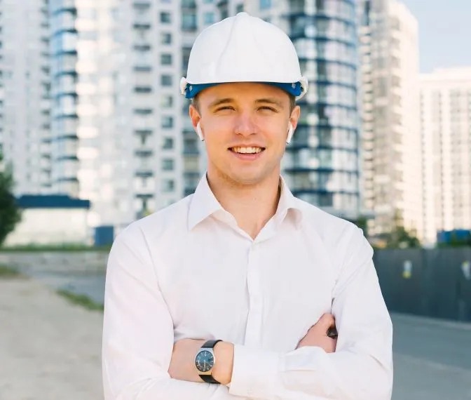 Construction project manager in a white hard hat in front of new apartment buildings