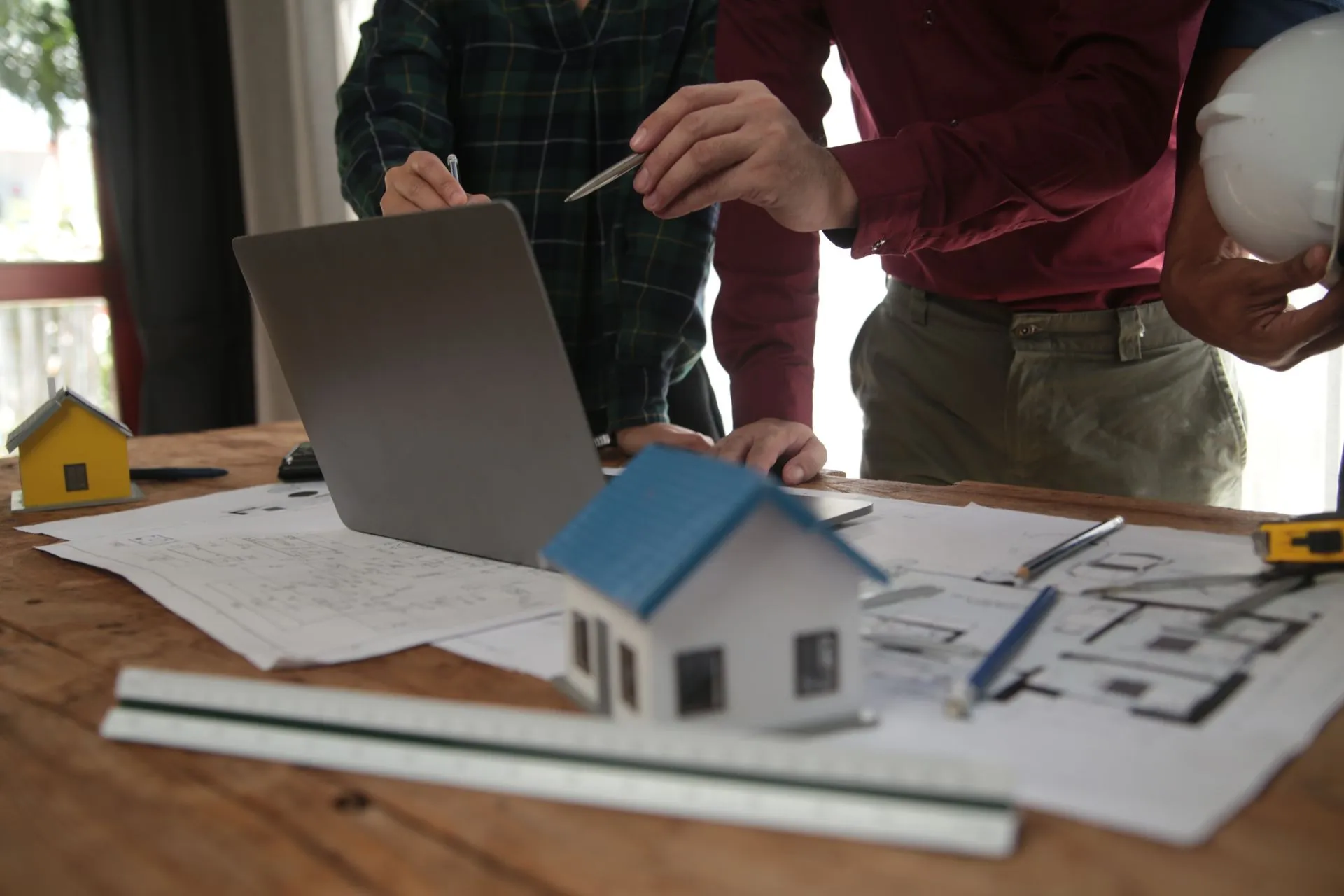 Builders walking clients through blueprints, a laptop and a house model at a table