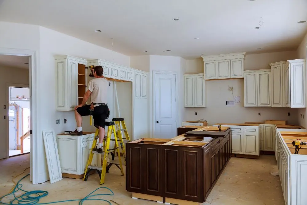 Installer on a ladder fitting antique white cabinets during a kitchen remodel